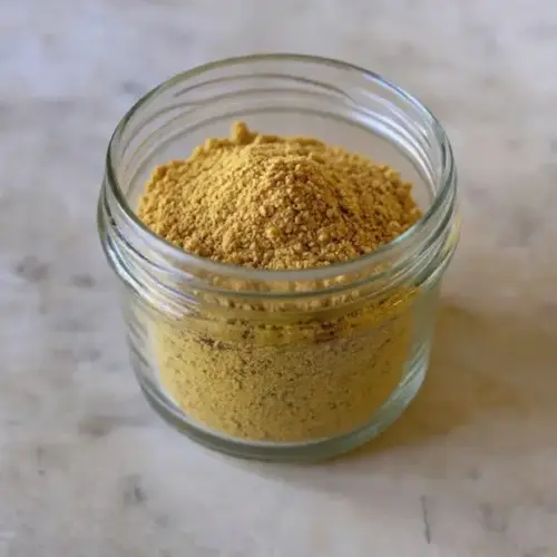 Chicken Bouillon Powder 8 Jar of homemade chicken bouillon powder with fresh herbs on a rustic wooden surface.
